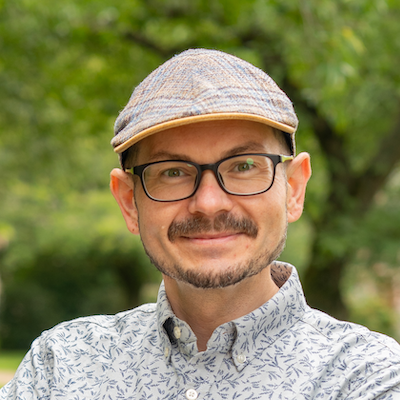 White man in early 40s wearing glasses and a newsboy cap.
